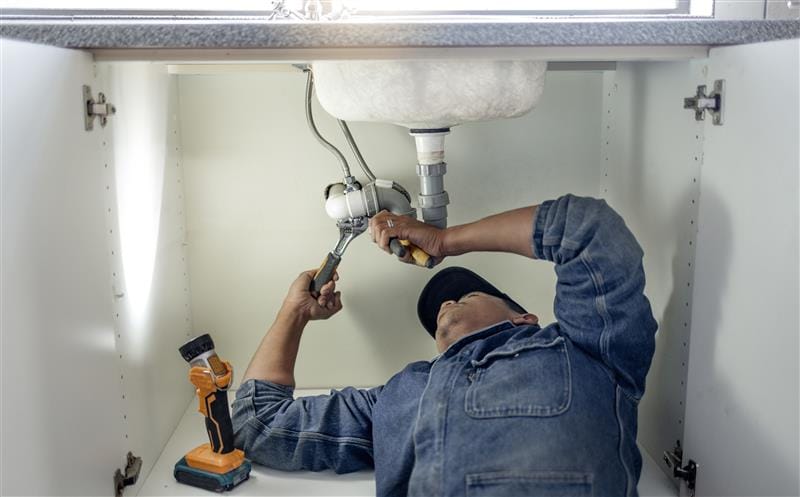 Plumber repairing pipes beneath a bathroom sink in Oregon City