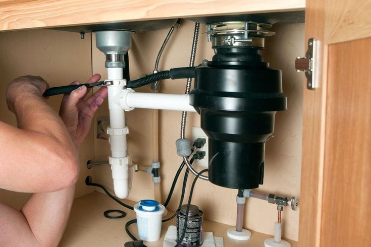 Plumber installing a garbage disposal beneath a kitchen sink in Oregon City