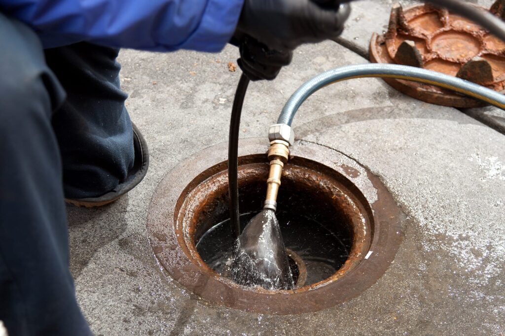 Plumber hydro jetting a sewer line through a manhole in Oregon City