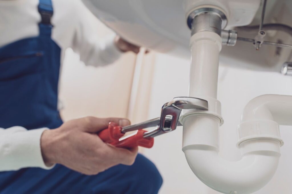 Plumber repairing a white drain pipe beneath a sink in Oregon City