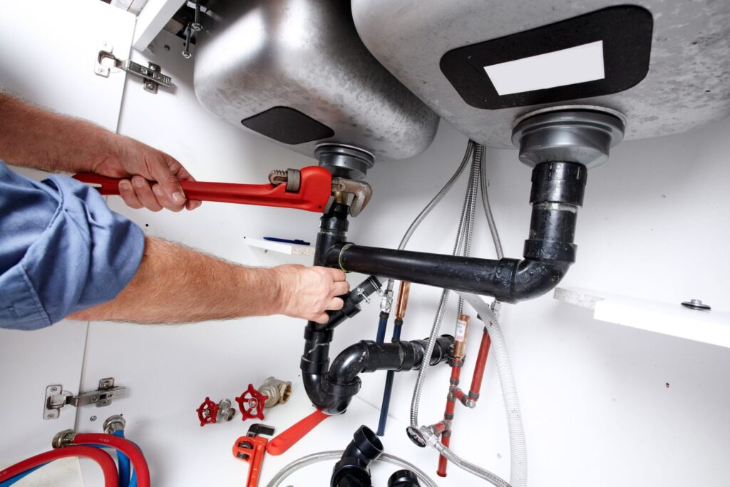Plumber repairing drain pipes beneath a kitchen sink in Oregon City